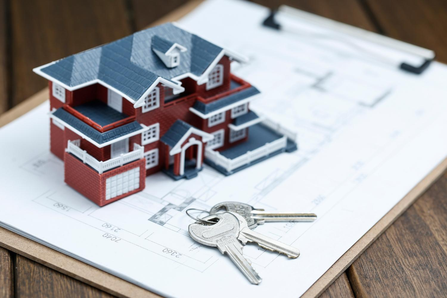 A miniature house with a key placed on a plan chart on a clipboard, which is kept on a table